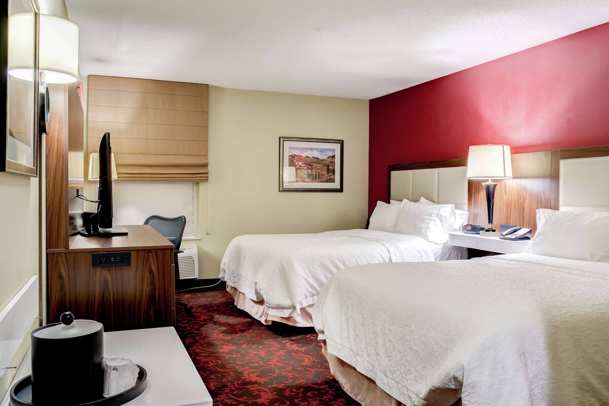 A hotel room with two beds, a desk with a computer, a television, and a painting on the wall.