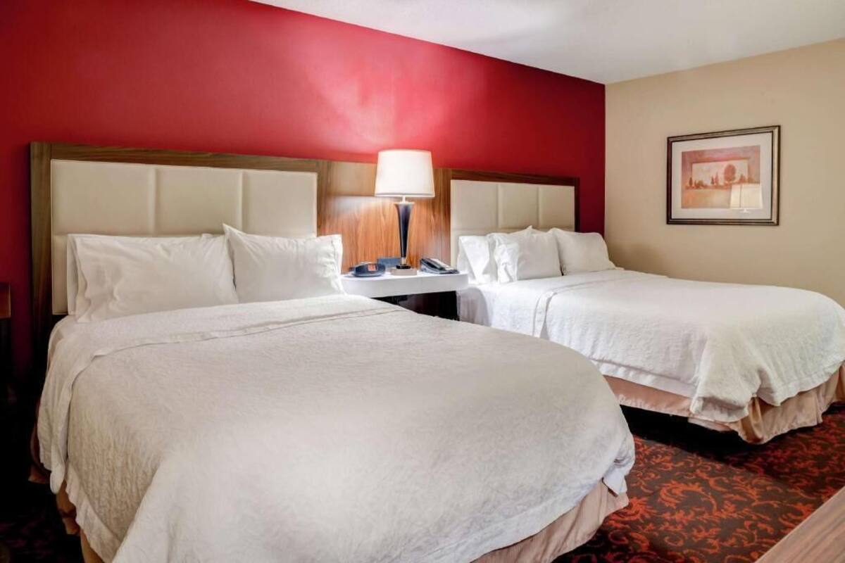 A hotel room with two beds, a nightstand with a lamp, and a framed picture on the wall.