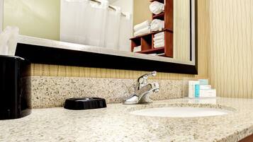 A bathroom with a granite countertop, a white sink, a silver faucet, a towel rack with folded towels, and a mirror reflecting the bathroom.
