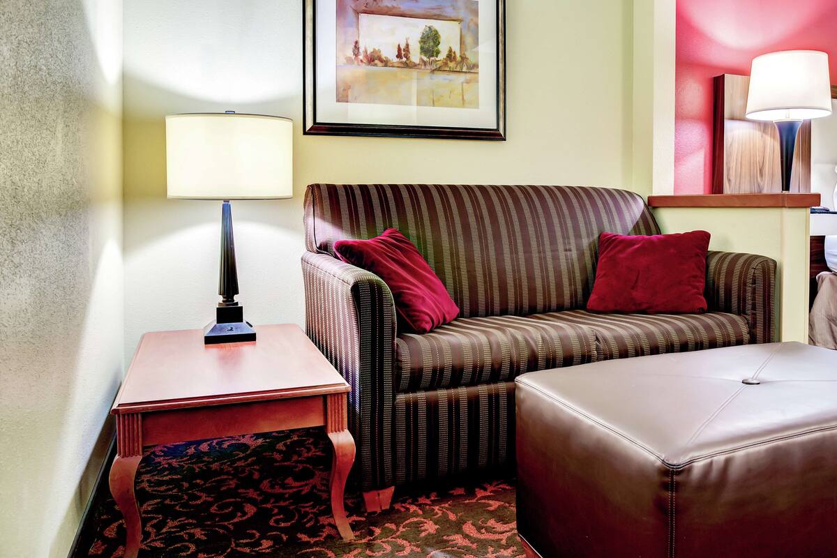 A living room with a striped sofa, a red cushion, a small table with a lamp, and a framed picture on the wall.