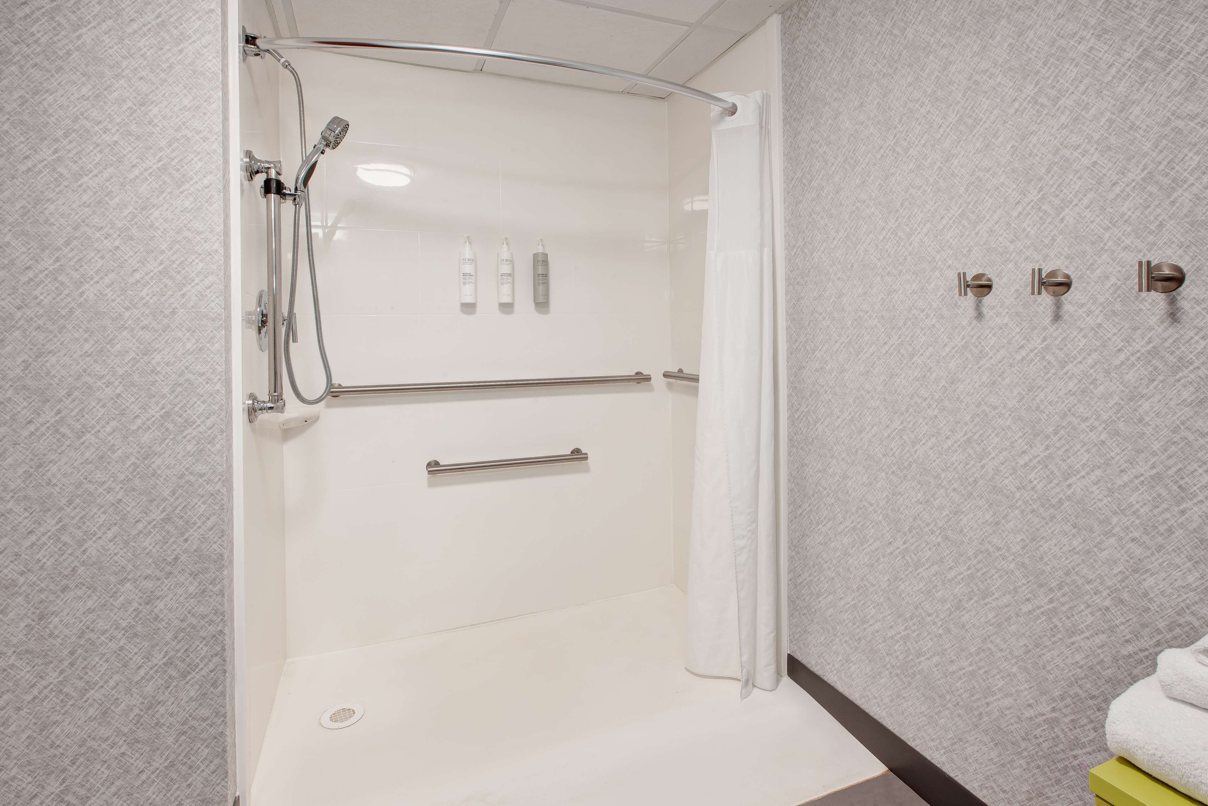 Un baño moderno con cabina de ducha, barras de apoyo y un perchero para toallas.