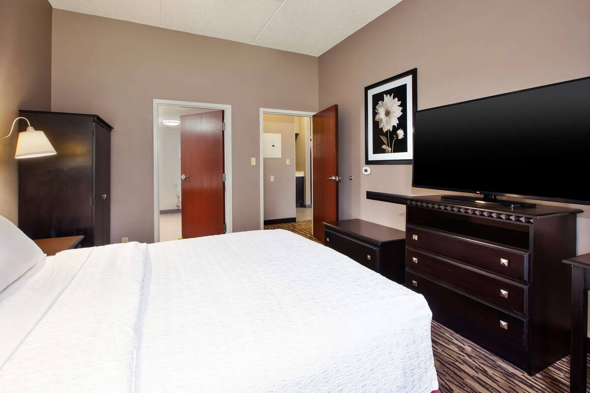 A hotel room with a large bed, a dresser, a TV, and a door leading to a bathroom.