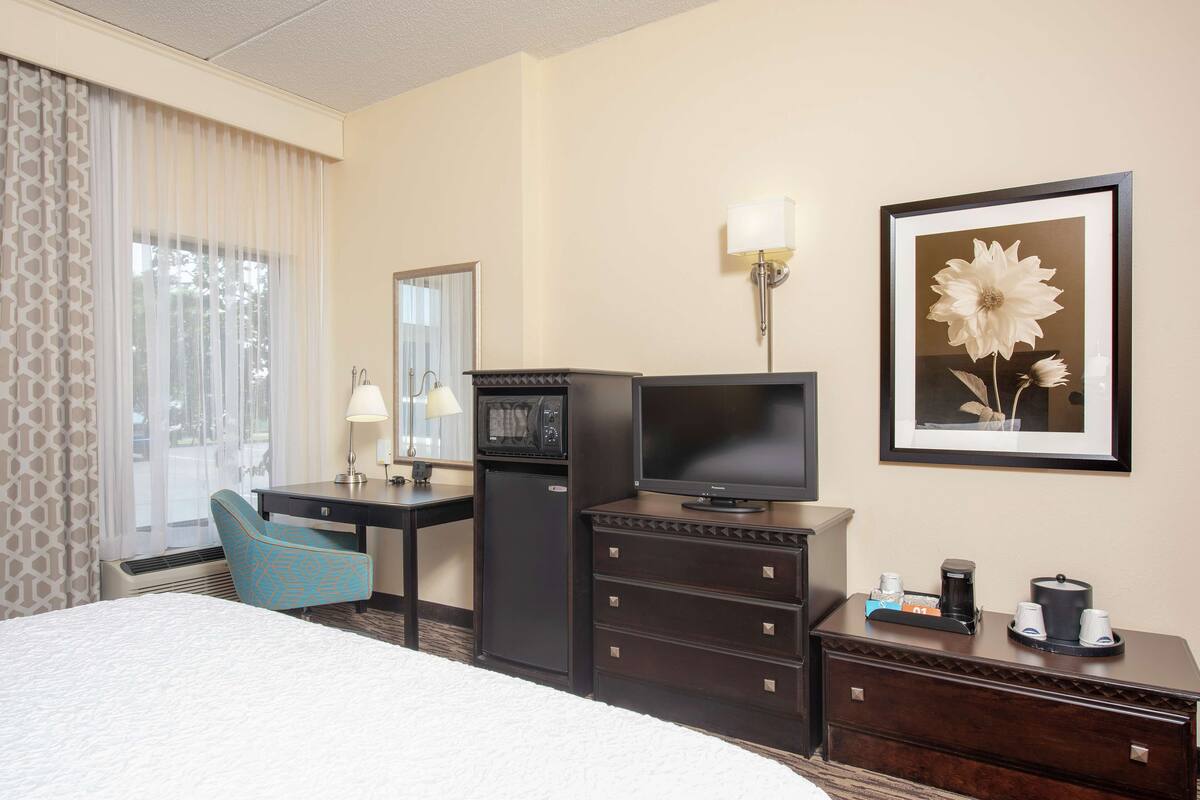 A hotel room with a bed, a desk with a computer, a TV, a coffee maker, and a framed picture on the wall.
