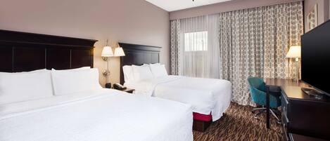 A hotel room with two beds, a desk, a chair, a TV, and a ceiling fan.