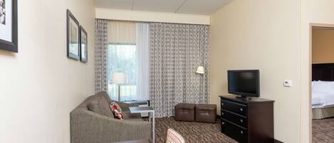 A hotel room with a sofa, a small table, a TV, a dresser, and a bed.