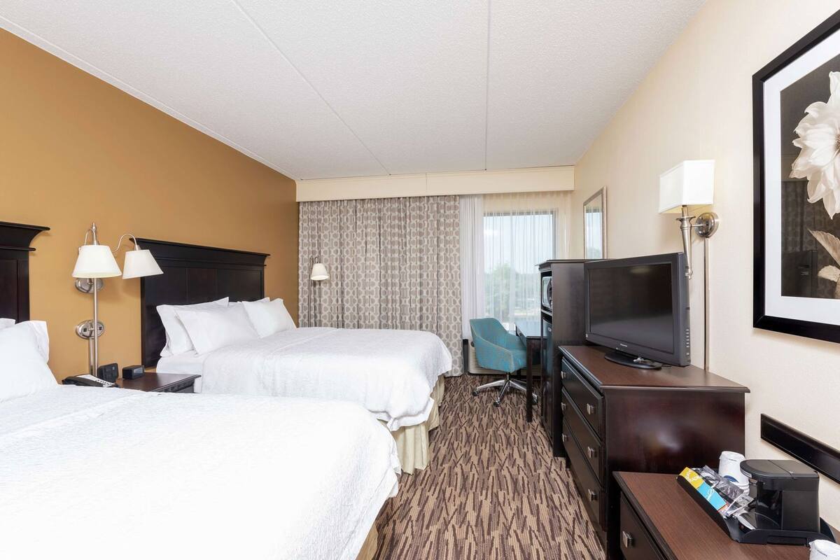 A hotel room with two beds, a desk with a television, a chair, and a coffee maker.