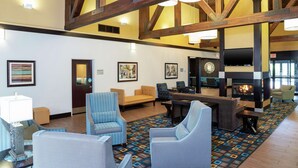 A spacious lobby with high ceilings, exposed wooden beams, and a fireplace. There are several seating areas with sofas and armchairs, and a patterned carpet.