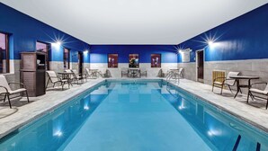 A swimming pool with lounge chairs and tables, surrounded by blue walls and a tiled floor.