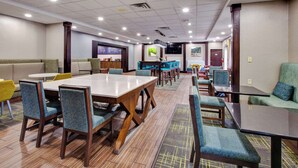 A hotel lobby with a large dining table, several chairs, a bar area, and a seating area with couches.