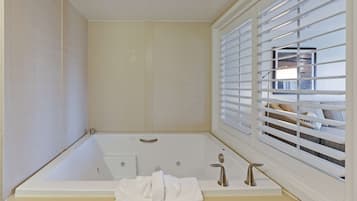 A bathroom with a bathtub, a window with blinds, and a towel on the floor.