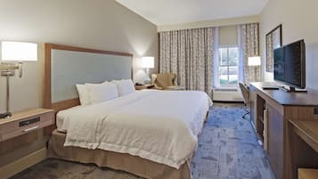 A hotel room with a large bed, a desk with a television, a chair, and a desk lamp.