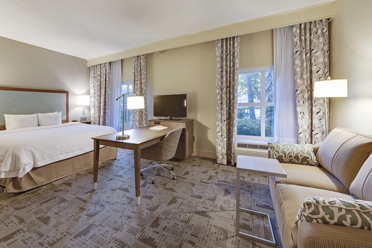 A hotel room with a bed, desk, chair, TV, and a sofa.