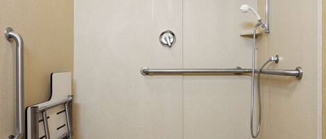 A handicap-accessible shower stall with a grab bar, a wheelchair lift, and a handheld showerhead.
