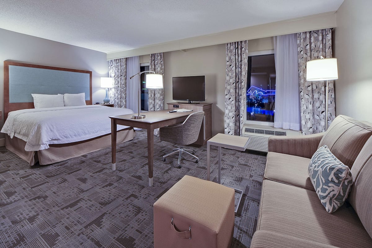 A hotel room with a bed, desk, chair, sofa, and a TV.