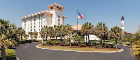 A hotel with a prominent American flag, palm trees, and a lighthouse in the background.