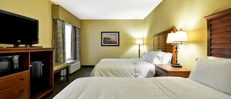 A hotel room with two beds, a television, a desk with a lamp, and a picture on the wall.