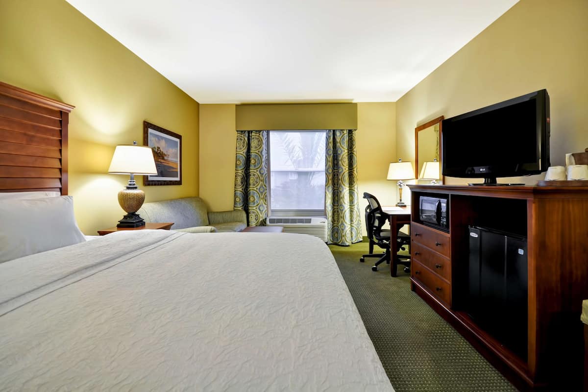 A hotel room with a large bed, a desk with a computer, a television, and a minibar.