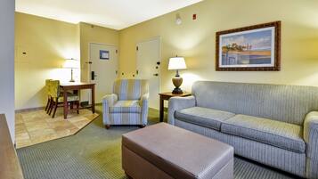 A hotel room with a sofa, armchair, small table, and lamp.