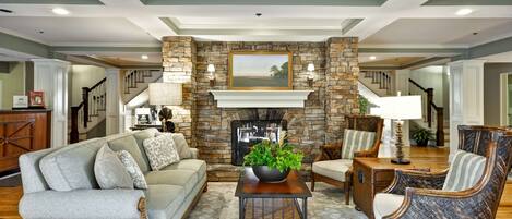A spacious living room with a stone fireplace, comfortable seating, and a staircase leading to other areas.