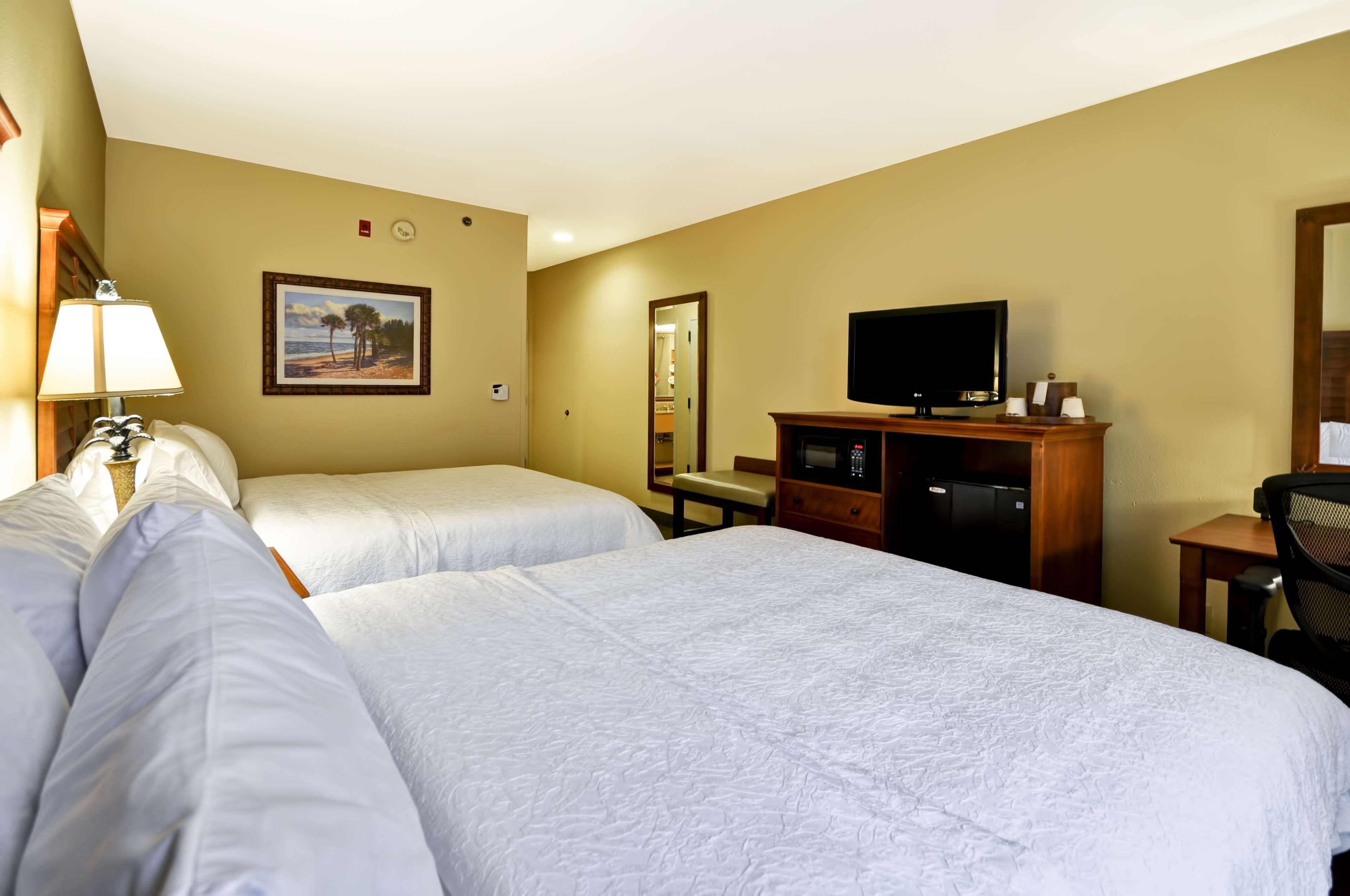 Una habitación de hotel con dos camas, televisión, escritorio y espejo.