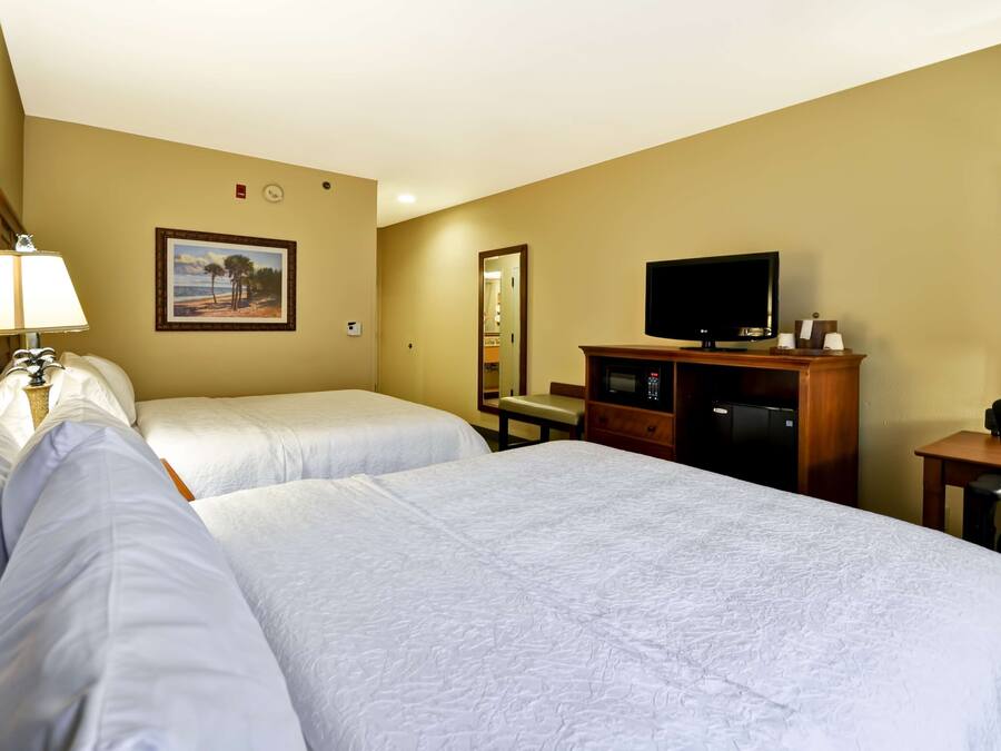 Una habitación de hotel con dos camas, televisión, escritorio y espejo.