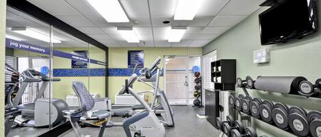 Un gimnasio con cintas de correr, elípticas y un estante de mancuernas.