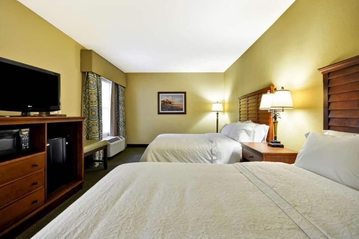 A hotel room with two beds, a TV, a desk with a lamp, and a picture on the wall.
