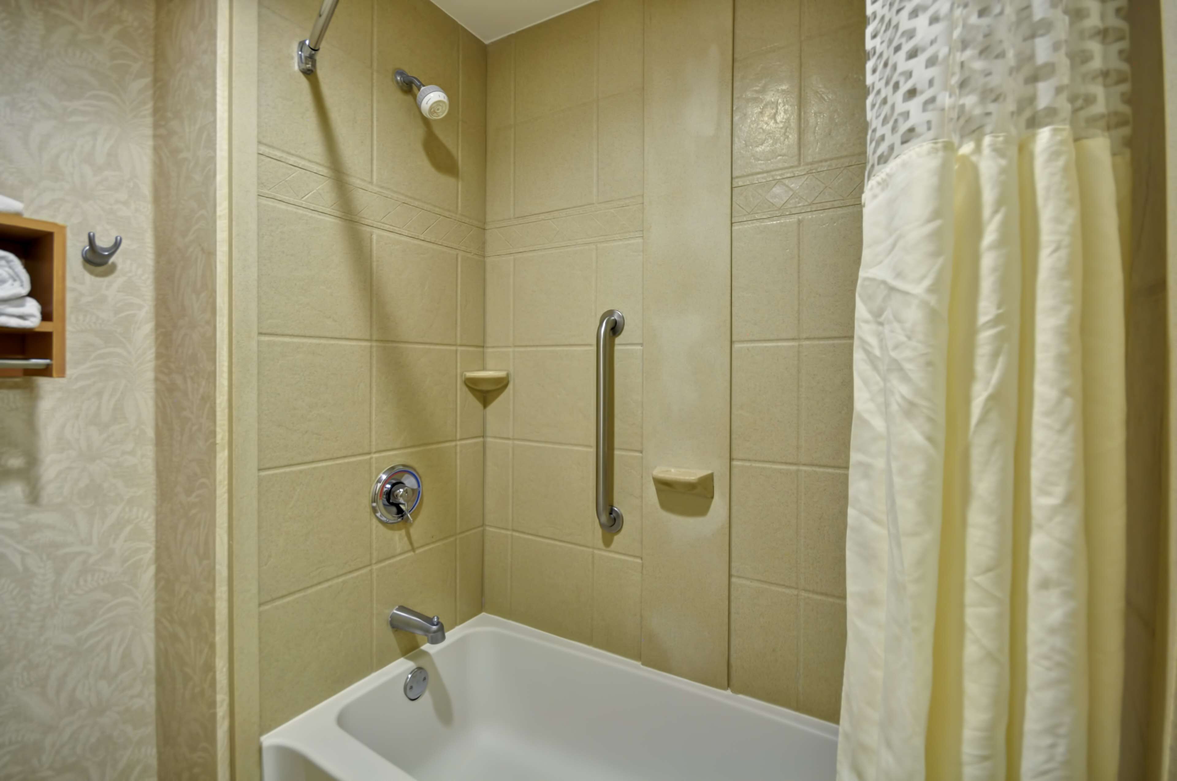 A bathroom with beige tiles, a bathtub, a shower with a handheld showerhead, and a towel rack.