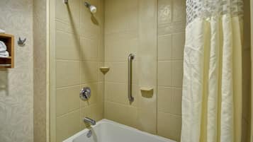 A bathroom with beige tiles, a bathtub, a shower with a handheld showerhead, and a towel rack.