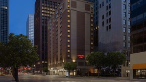 Un hotel con un cartel llamativo de 'Hampton Inn', rodeado de edificios altos y una calle despejada.