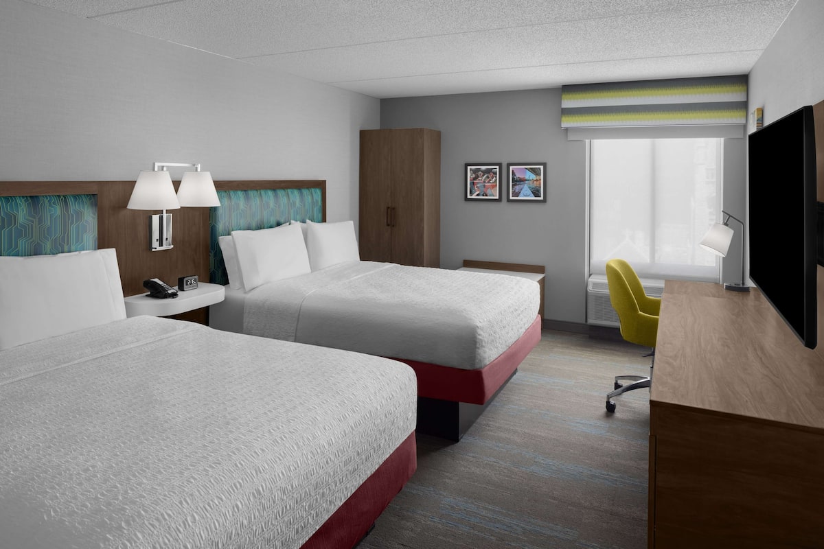 A hotel room with two beds, a desk, a chair, a TV, and a window with a view.