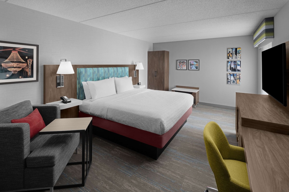 A hotel room with a bed, a desk, a chair, a sofa, and a TV.