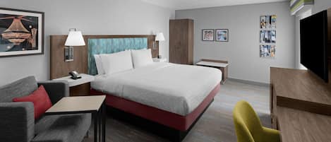 A hotel room with a bed, a desk, a chair, a sofa, and a TV.