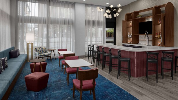 Una habitación de hotel moderna con una zona de bar, asientos y un ventanal con cortinas translúcidas.