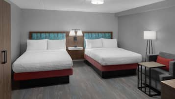 Quarto de hotel com duas camas, mesa de cabeceira, abajur e uma pequena mesa.