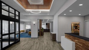 A modern hotel lobby with a wooden reception desk, a blue carpeted area, and a view into the dining area. - Hampton Inn Cleveland-Downtown (Cleveland)
