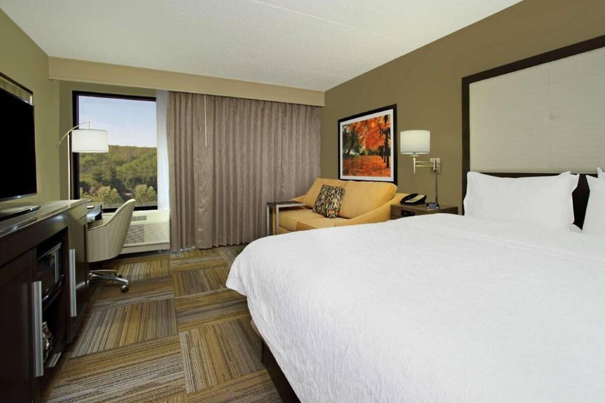 A hotel room with a large bed, a desk with a chair, a television, and a window with curtains.