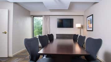 A conference room with a long table, six chairs, a flat-screen TV, a lamp, and a window with curtains.