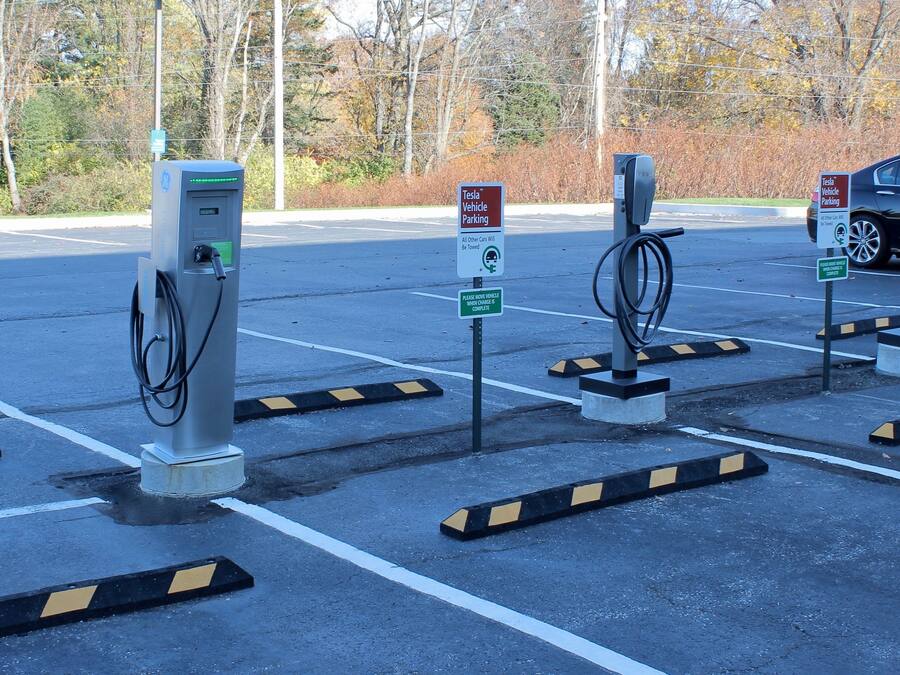 A parking area with multiple electric vehicle charging stations, signs indicating Tesla vehicle parking, and a sign instructing to move the vehicle when charging is complete.