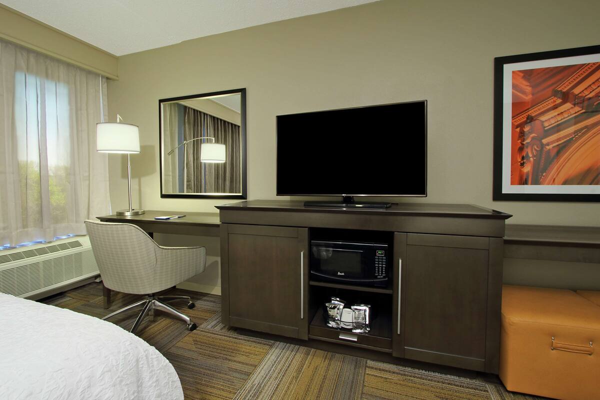 A hotel room with a bed, a desk with a flat-screen TV, a microwave, a chair, and a small seating area.