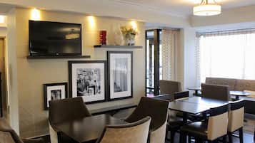 A dining area with a TV mounted on the wall, framed pictures, and a vase with flowers.
