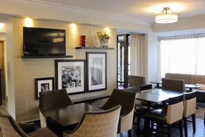 A dining area with a TV mounted on the wall, framed pictures, and a vase with flowers.