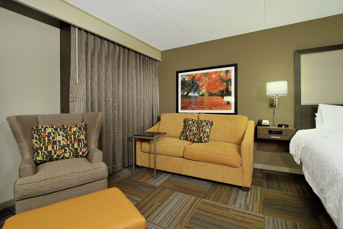 A hotel room with a sofa, armchair, and a small table.