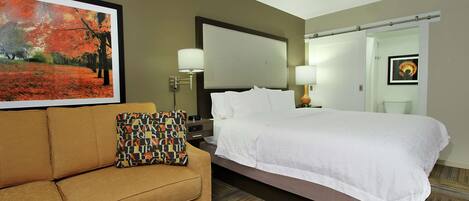 Una habitación de hotel con una cama, un sofá, un cuadro y una lámpara.