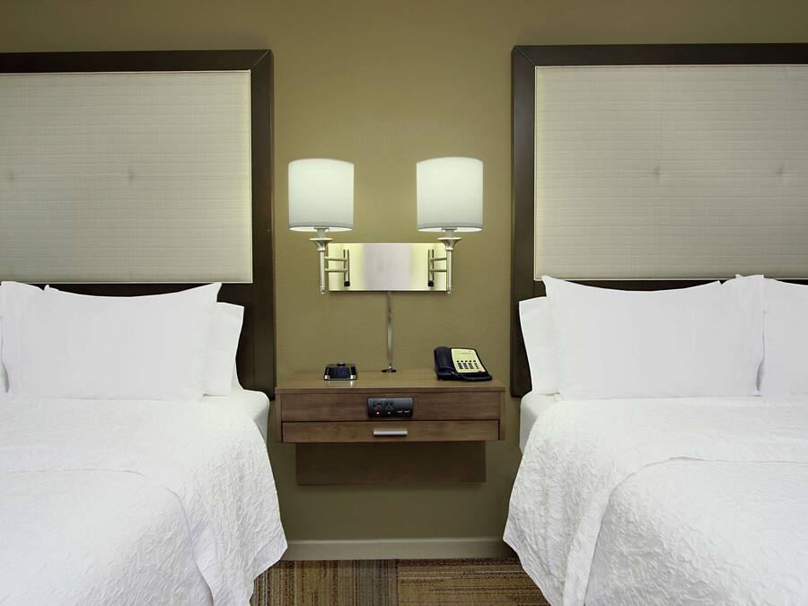 Une chambre d’hôtel avec deux lits, une table de chevet avec une lampe, un téléphone et une petite table.