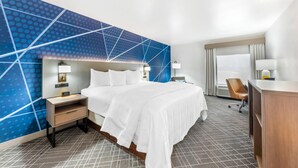 A hotel room with a large bed, a desk, a chair, and a blue patterned wall.