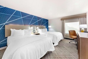 Two single beds with white linens, a geometric-patterned wall, and a large window with curtains.