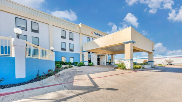 A Comfort Inn hotel with a covered entrance, a parking lot, and a clear blue sky.
