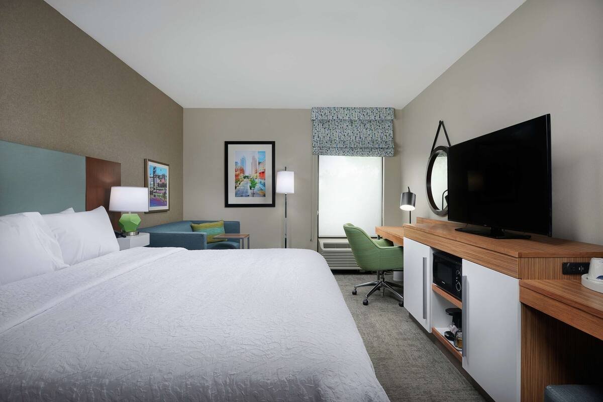 Habitación de hotel con una cama grande, un escritorio con computadora, televisión y ventana con vistas.