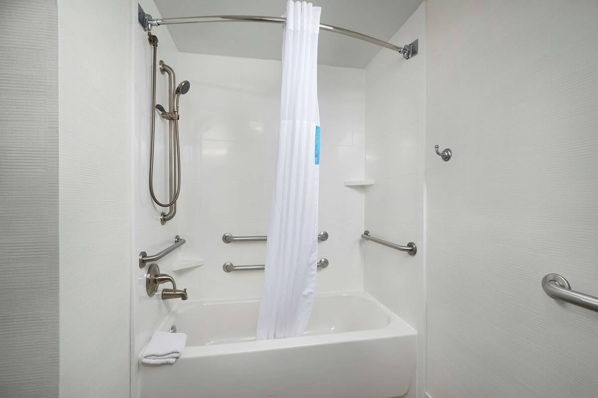 A white bathtub with a showerhead, grab bars, and a towel.